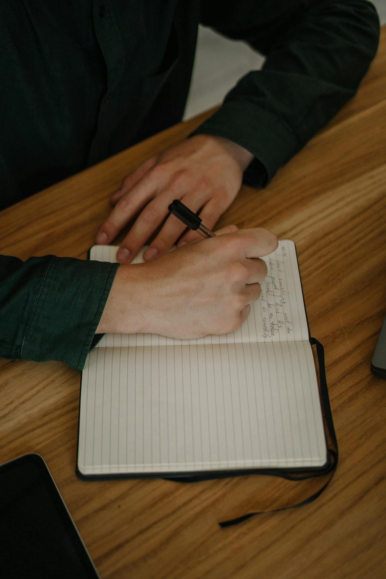 Image of a men writing on a diary, keeping notes for things to do on a wooden desk showing a sincere, handwritten letter or note.