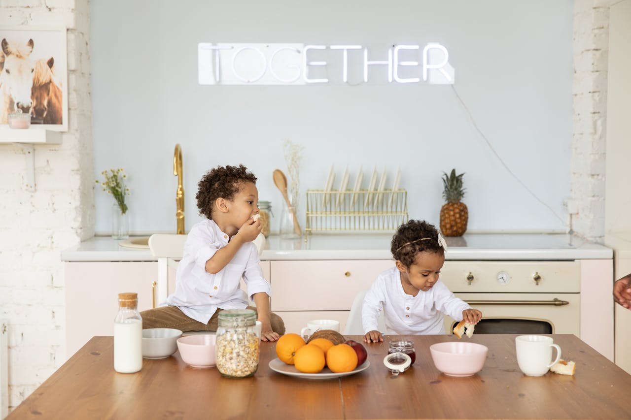 How Can a Mother Manage Work-Life Balance? Image of two young kids in a kitchen eating breakfast with milk, cereal, and fruit on a wooden table.