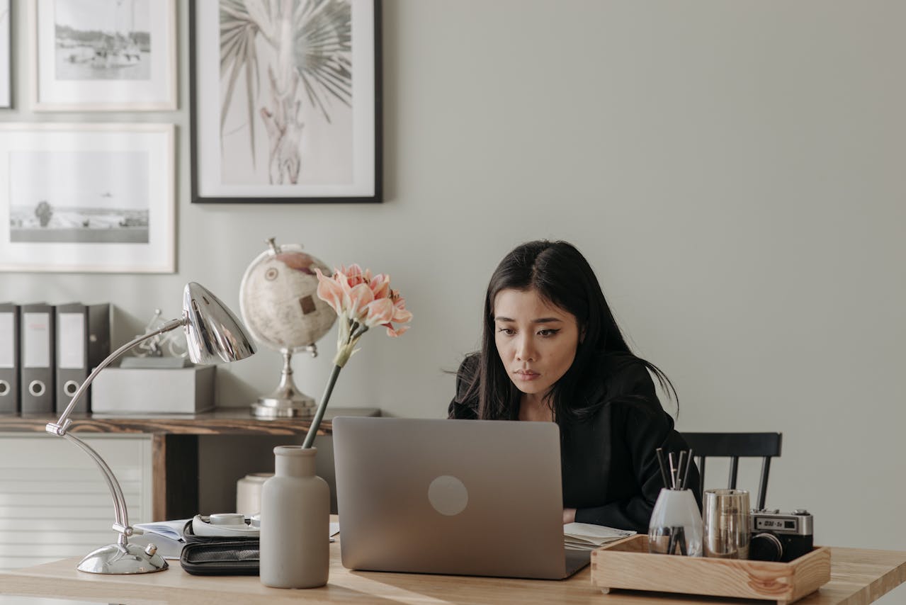 How Can a Mother Manage Work-Life Balance? Image of a woman working on a laptop at a desk with flowers, globe, and modern office decor.