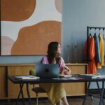 Image of a woman at desk with laptop, colorful clothes on rack, large abstract wall art behind her, showing how working women can find work-life balance.