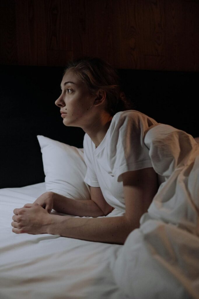 Image of a woman in a white t-shirt lying awake in bed at night, staring thoughtfully into the distance, showing why mornings are challenging if you have depression.