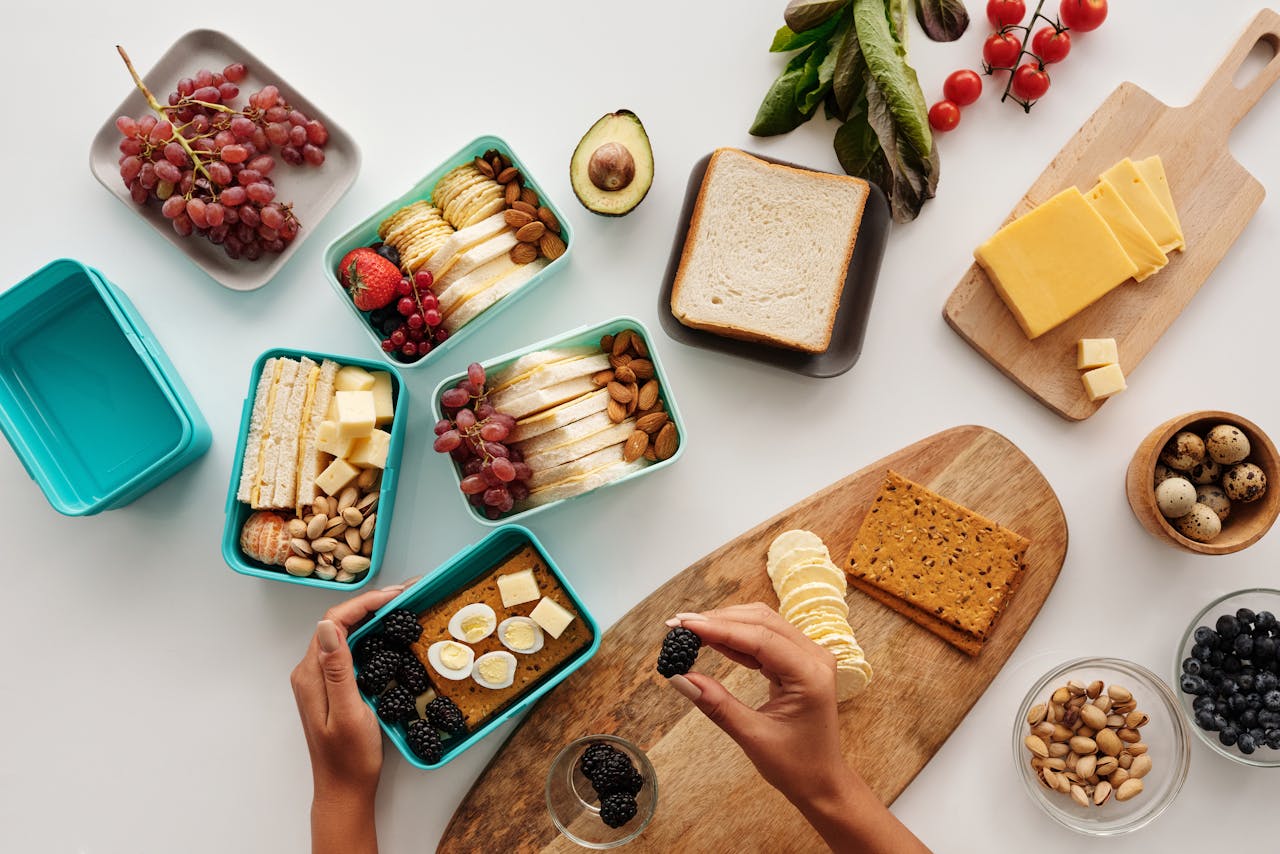 How Can a Mother Manage Work-Life Balance? Image of a hands preparing healthy lunchboxes with fruits, nuts, cheese, and sandwiches on a table.