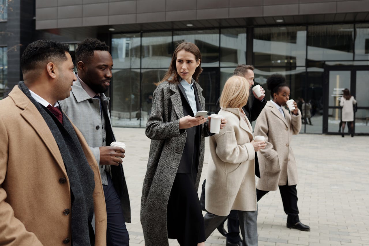 How Women Working in Demanding Careers Can Make Time for Physical Wellness? Image of a group of professionals walking outside with coffee cups, wearing winter coats, mid-conversation.