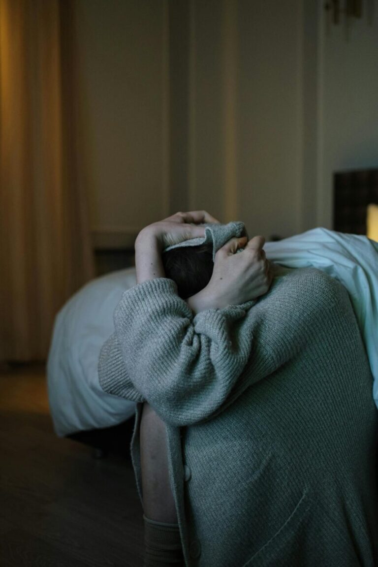 Image of a woman crouching on the floor near a bed, hiding face in sweater, appearing distressed, showing can you get depressed without having depression.