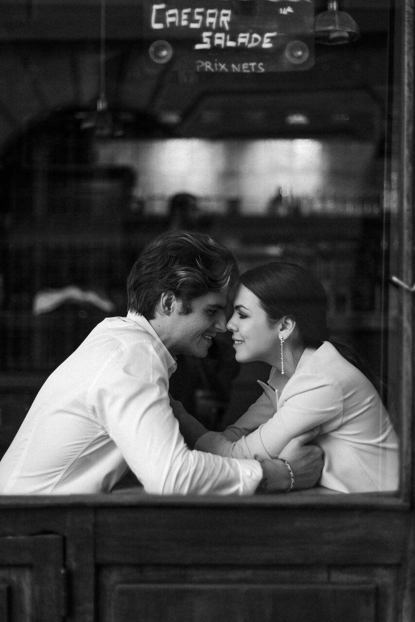 Invisible String Theory: Is It Real and Does It Work? Image of a romantic couple smiling and leaning close to each other in a cozy café, seen through the window.