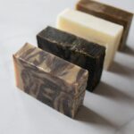 Image of a four handmade soap bars of different colors arranged diagonally on a white marble surface, representing what is antibacterial soap good for.