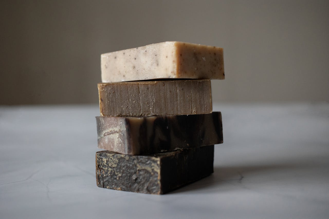 How to Keep Your Vagina Clean and Smelling Good? Image of a stack of five handmade soap bars in natural tones on a smooth grey surface with soft lighting, representing how to keep your vagina clean and smelling good.