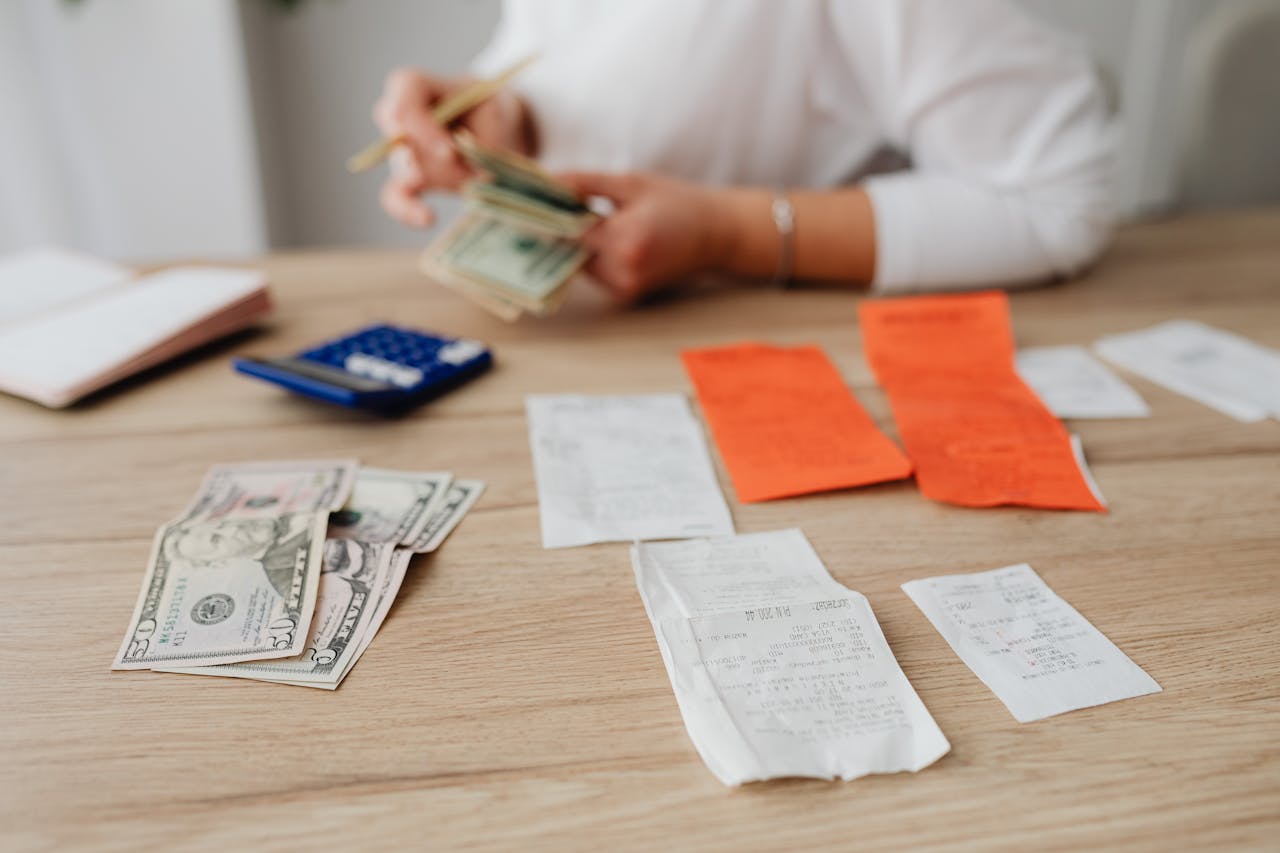 How to Survive Being a Stay at Home Mom Financially? Image of a woman counts cash with receipts and a calculator on a wooden table while organizing finances, representing how to survive being a stay at home mom financially.