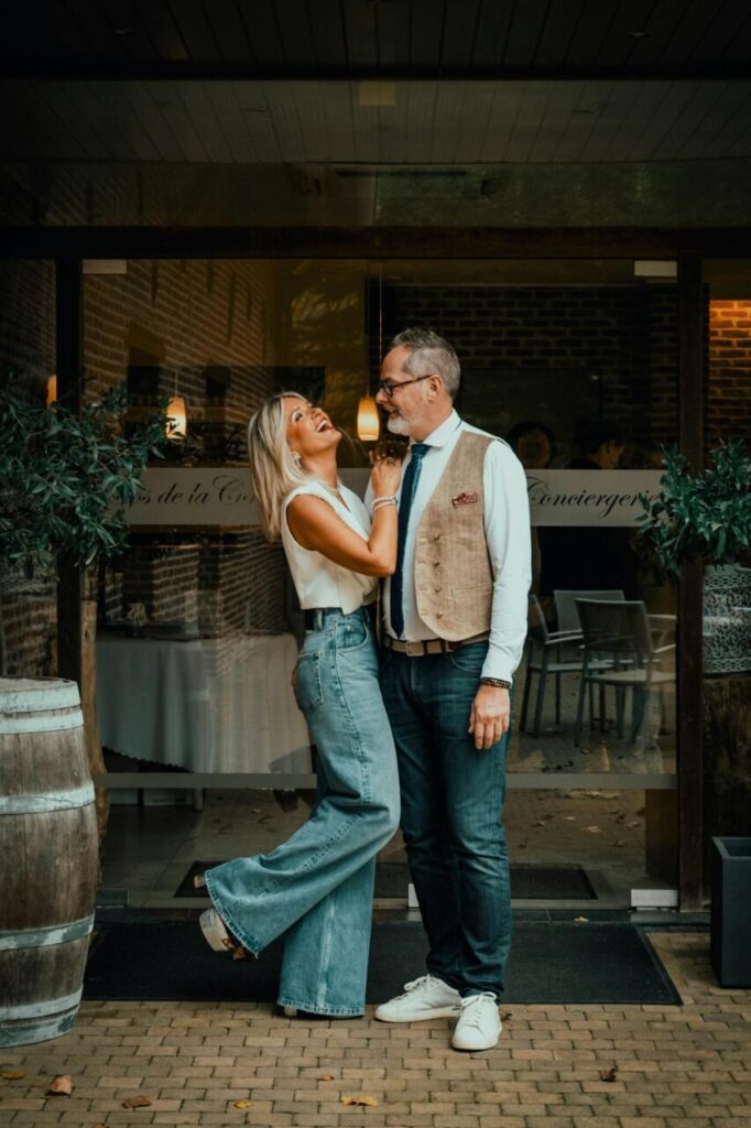 Image of a joyful couple stands close outside a restaurant, smiling and gazing lovingly at each other, showing invisible string theory.