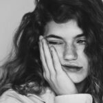 Image of a young woman with curly hair resting her face on her hand, looking tired or contemplative, showing fatherless daughter syndrome.