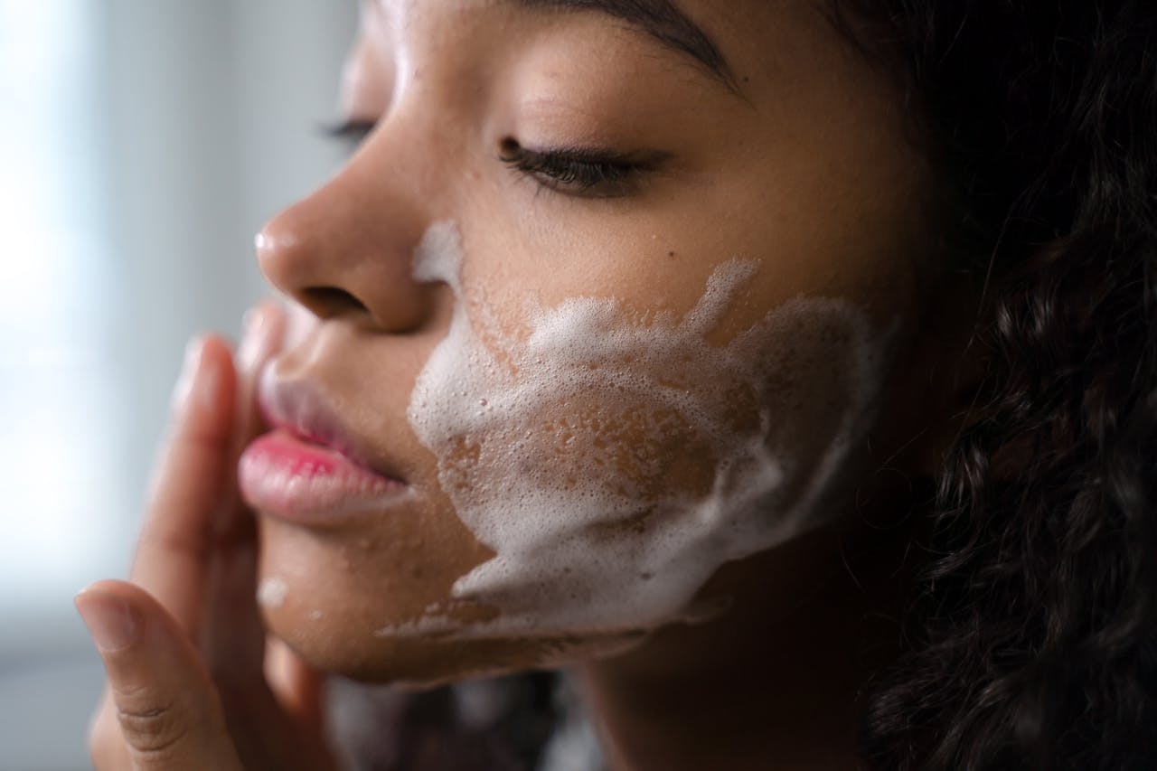 Image of a woman gently applying foamy cleanser to her cheek during a skincare routine.