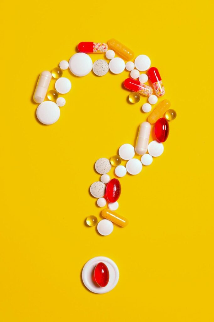 Image of assorted pills and capsules arranged in the shape of a question mark on a yellow background, showing is glutathione safe during pregnancy?