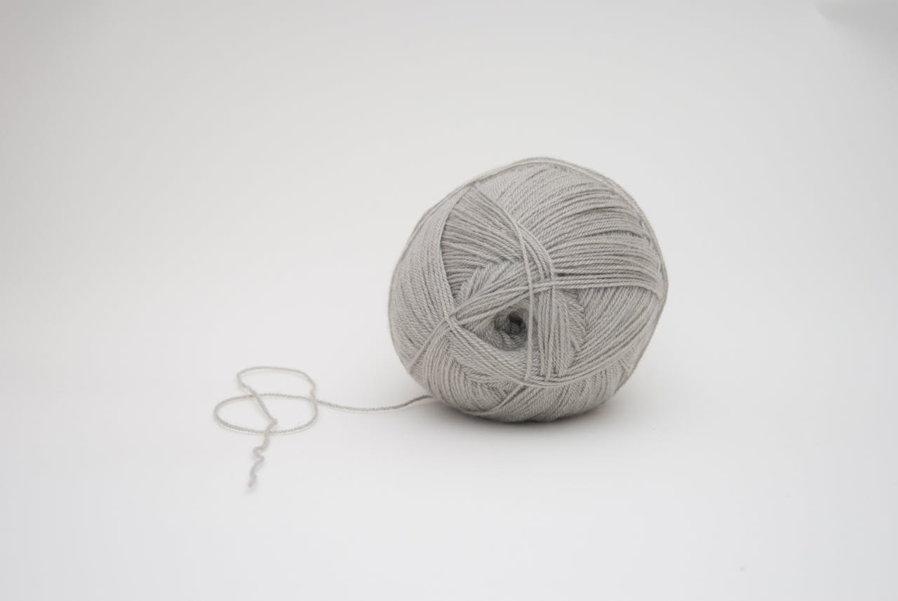Invisible String Theory: Is It Real and Does It Work? Image of a neatly wound ball of light gray yarn with a loose end resting on a white background, representing invisible string theory.