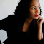Image of a woman in black outfit with red lipstick gazing thoughtfully to the side, hand on chin, showing how to break generational trauma.