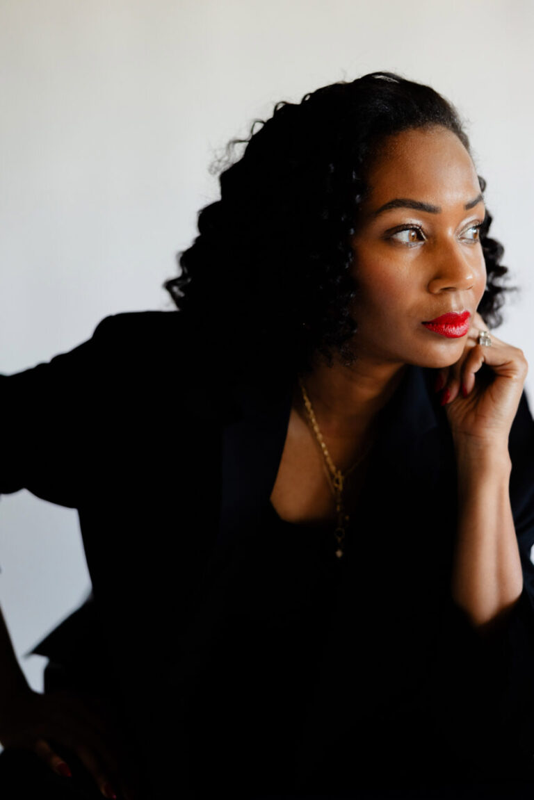 Image of a woman in black outfit with red lipstick gazing thoughtfully to the side, hand on chin, showing how to break generational trauma.