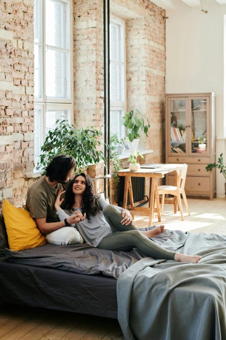 Image of a couple cuddling on a bed in a cozy loft with brick walls, plants, and natural sunlight, showing phrases to set boundaries with family.