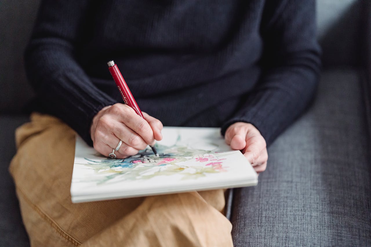 210 Best Hobbies for 60 Year Old Woman Image of a women sketching colorful artwork on a sketchpad while sitting on a couch with relaxed posture.
