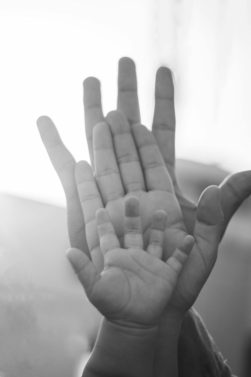 How to Break Generational Trauma: 5 Steps You Can Take Today Black-and-white photo of three overlapping hands: adult, child, and baby, palms facing camera, representing how to break generational trauma.