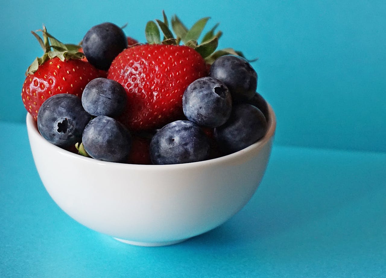 Image of a fresh strawberries and blueberries in a white bowl placed on a bright blue surface, responsibilities of a parent