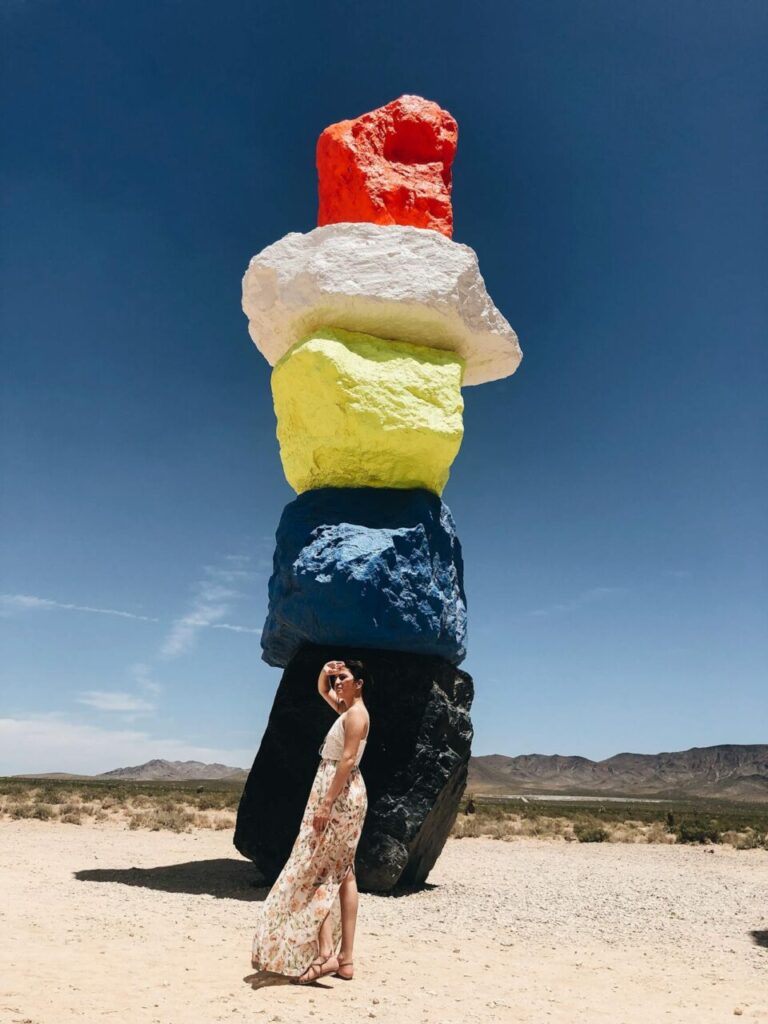 Image of a woman in a floral dress posing near a tall colorful rock sculpture in a desert landscape, showing clothes to wear in Las Vegas.