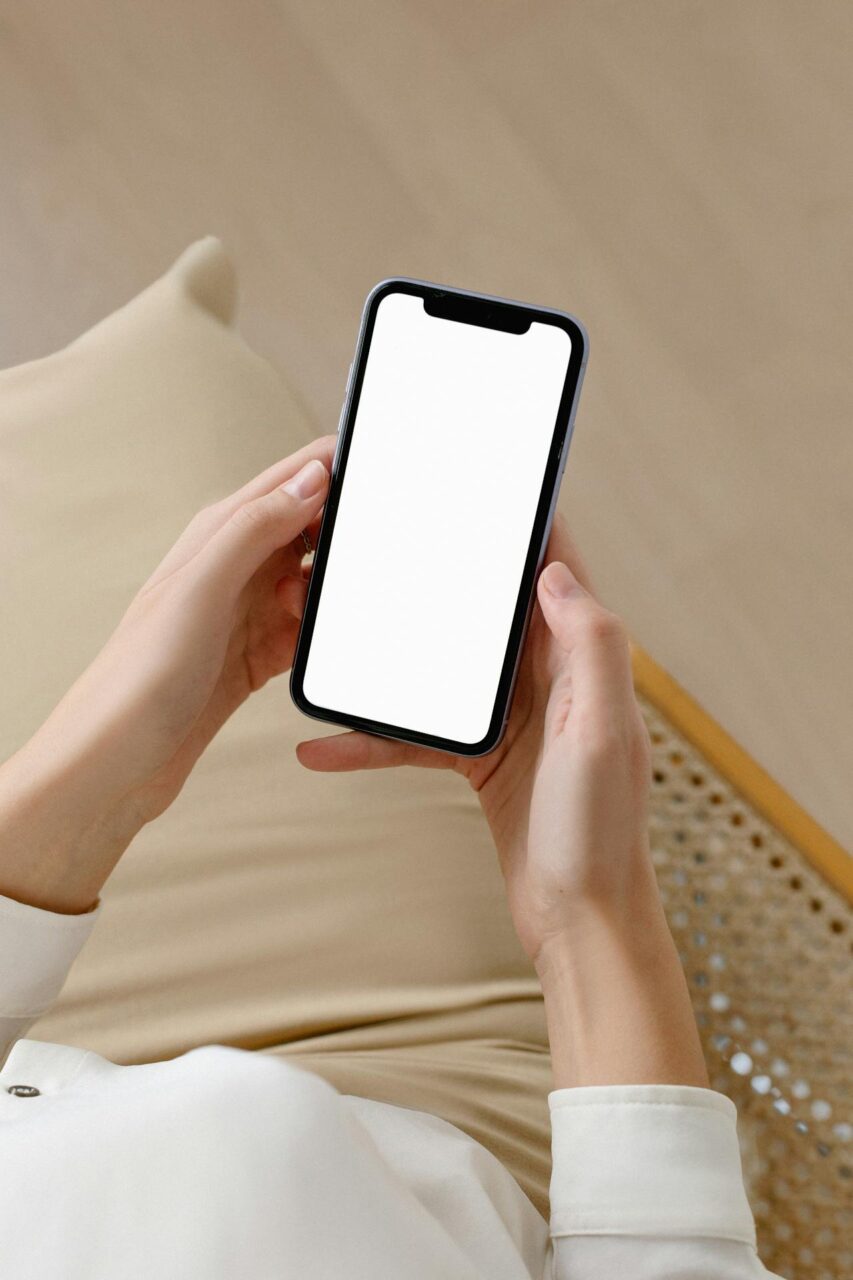 Image of a woman holding a smartphone with a blank white screen while sitting on a chair.