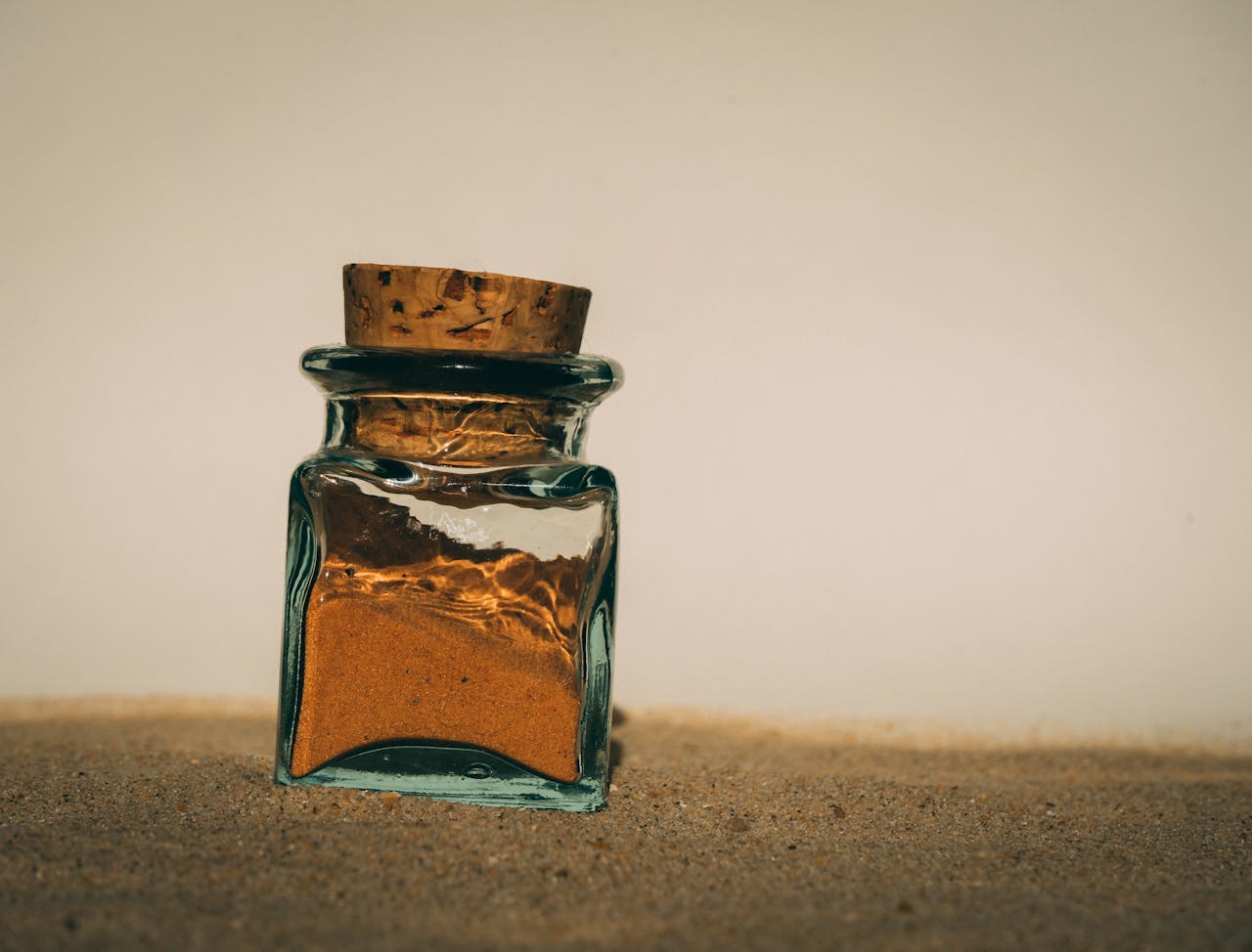 Image of a small glass jar filled with sand and sealed with a cork, placed on a sandy surface under soft light, representing gift for your daughter in law.