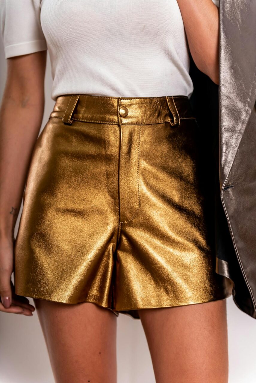 Image of a woman in shiny gold shorts and white top, holding a silver jacket to the side, representing cargo type shorts for women.