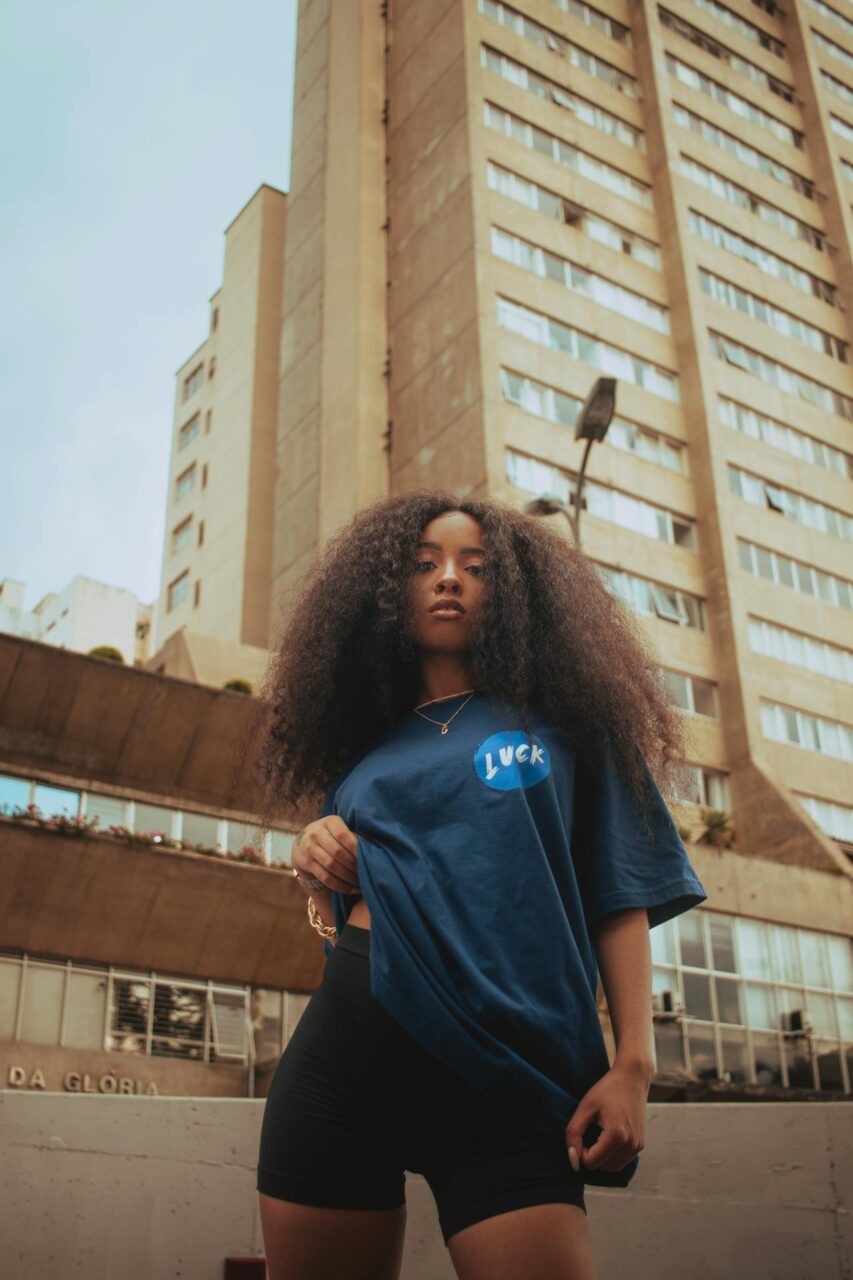 Image of a woman in blue t-shirt and black shorts standing confidently in front of tall buildings, showing types of shorts for different body types.