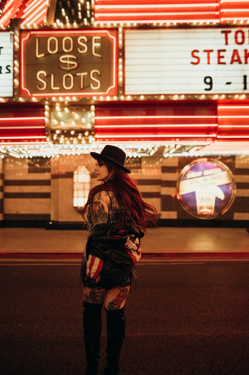 Image of a woman in stylish outfit with tattoos walking under bright neon casino lights at night in Las Vegas.