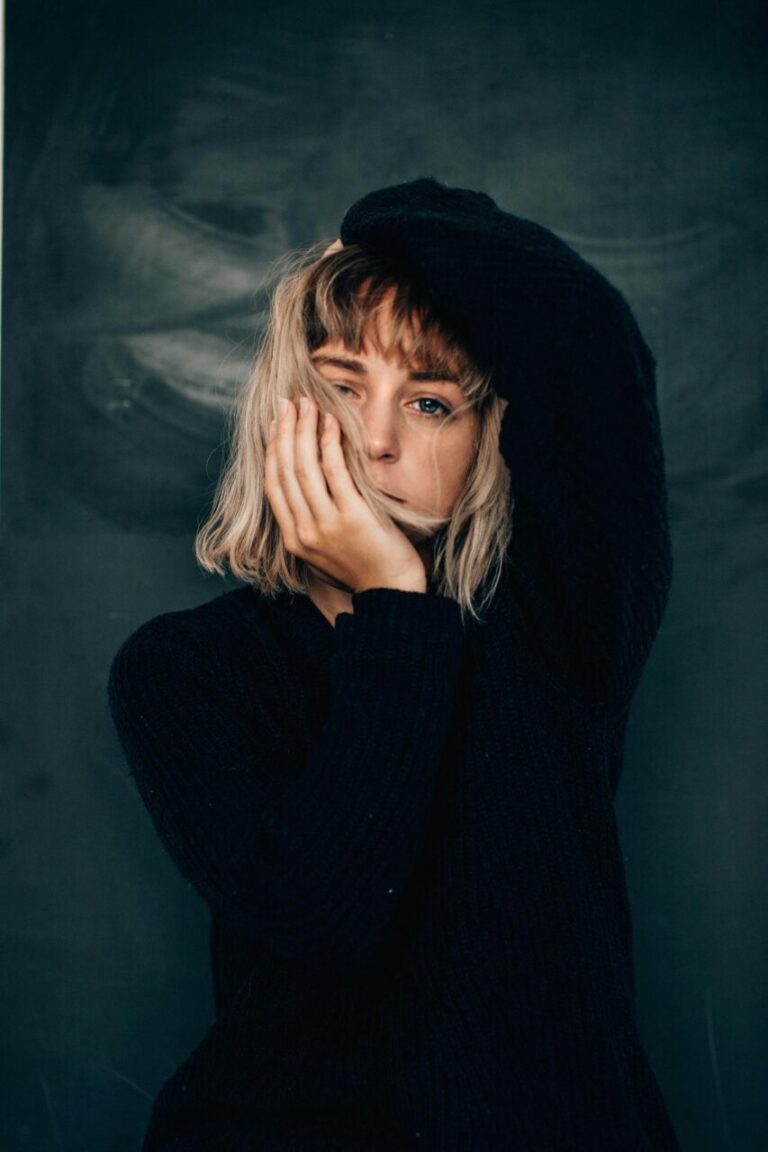 Image of a woman in black sweater resting her face on hand, looking pensive against dark background, showing can you forgive someone and still be hurt.
