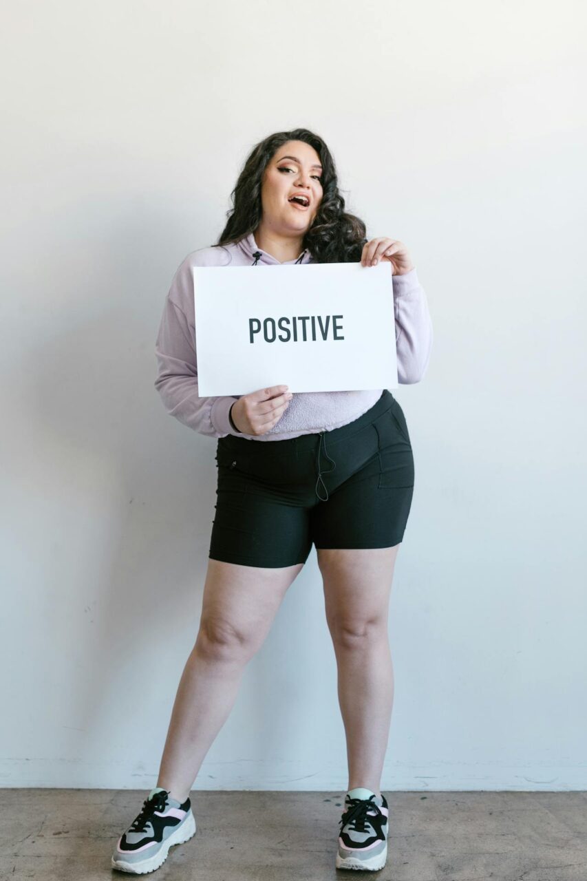 Image of a woman in casual outfit holding a white sign with the word, POSITIVE printed in bold.
