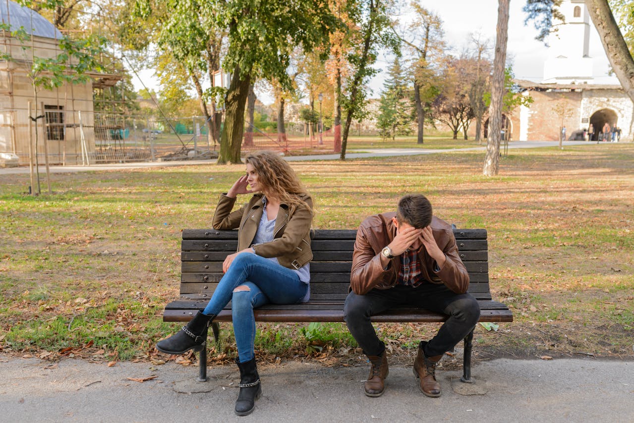 Image of a upset couple sitting apart on a bench in park, both appearing emotionally distressed.