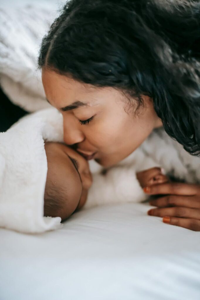 Image of a mother lovingly kisses her swaddled baby on the forehead while lying together on a cozy bed, showing how to be a successful single mom.