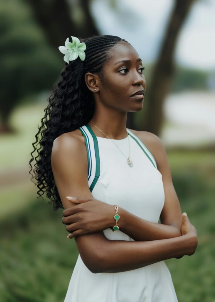 Image of a woman in white dress with green flower in hair, standing outdoors with folded arms, showing what to wear in South Africa for ladies.