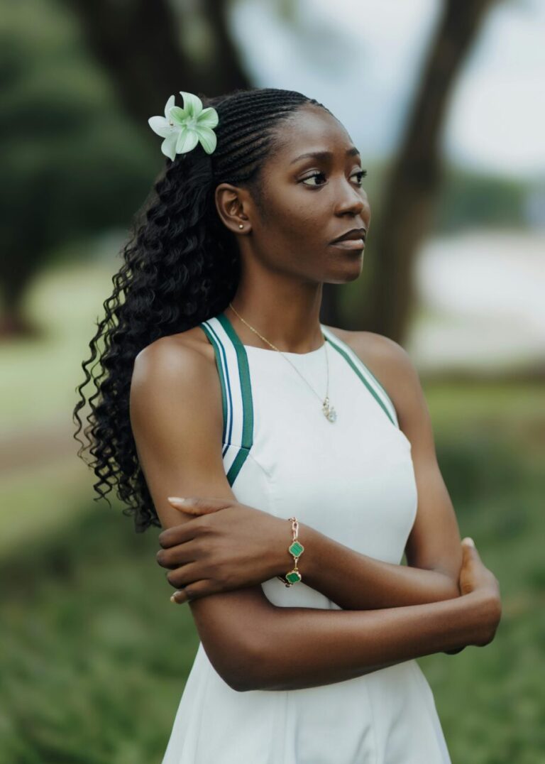 Image of a woman in white dress with green flower in hair, standing outdoors with folded arms, showing what to wear in South Africa for ladies.