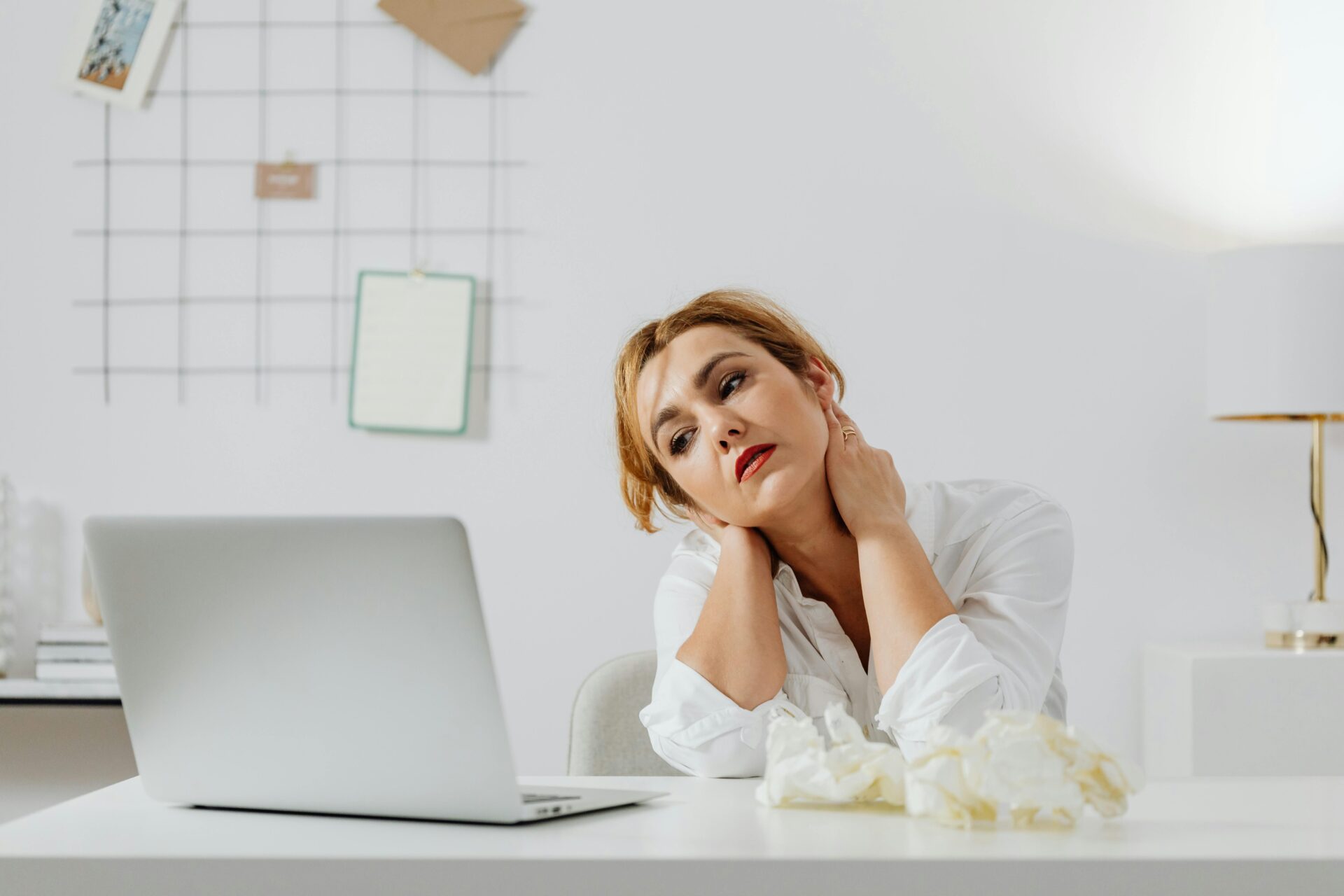 Image of a woman sitting at desk with laptop, holding her neck in discomfort, surrounded by crumpled tissues, showing how to figure out what to do with your life.
