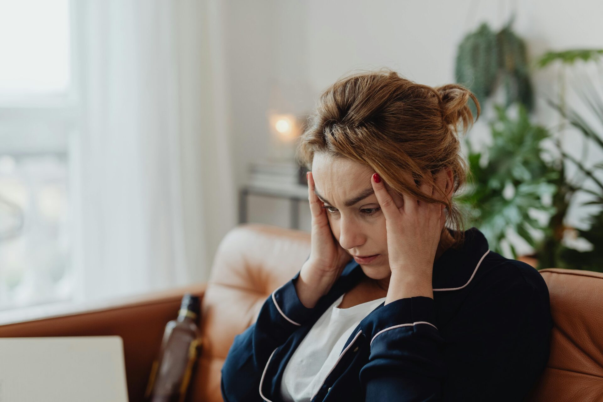 Image of a worried woman sits on a couch holding her head with both hands, appearing stressed and anxious, showing what to do when you feel overwhelmed with life.
