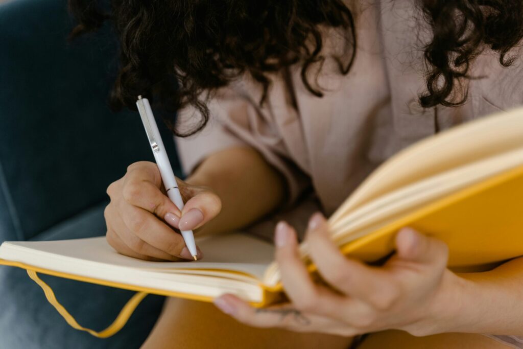 Image of a woman with curly hair writes in a yellow notebook while holding a pen in her hand, representing how to find direction in life.