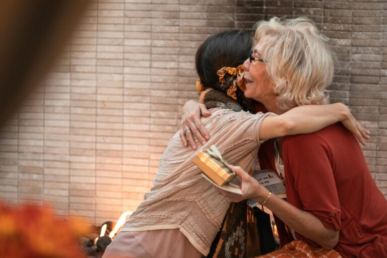 Image of a elderly woman hugging a younger woman warmly while holding a wrapped gift in her hand, showing presents for old people.