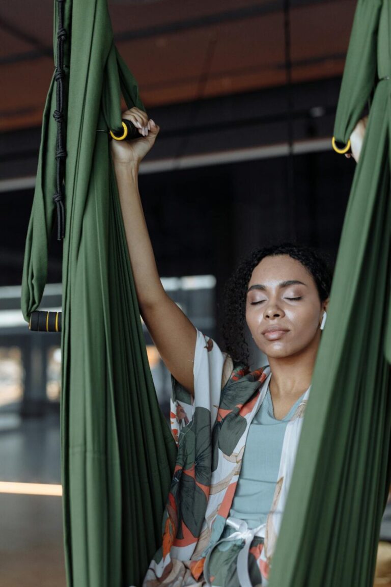 Image of a woman with closed eyes practices aerial yoga, holding green fabric hammocks in a calm studio, showing zoning out vs dissociation.
