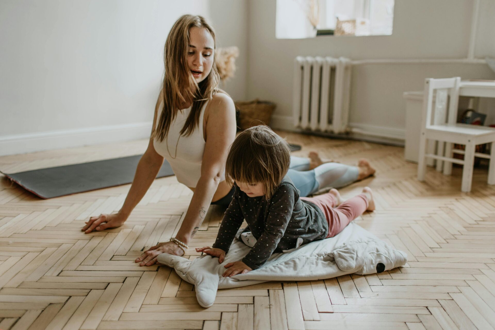 Image of a woman and child lying on the floor doing yoga together, the child imitating the cobra pose, showing 10-minute wellness activities.