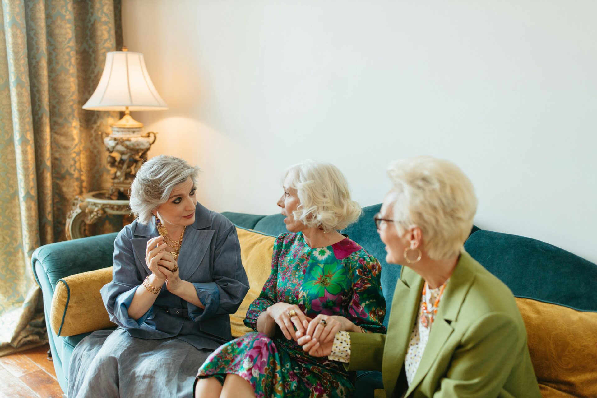 Image of three elderly women sitting on a sofa, talking and laughing while holding hands, representing activity gifts for old people.