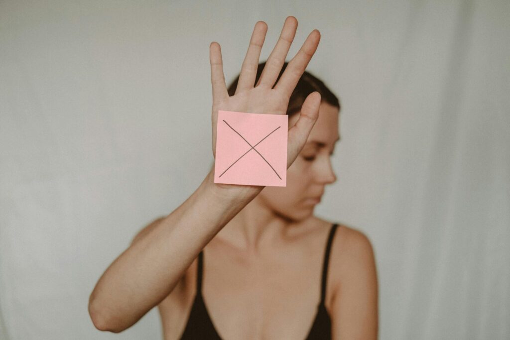 Image of a woman holds up her hand with a pink sticky note marked with an X, turning her face away.