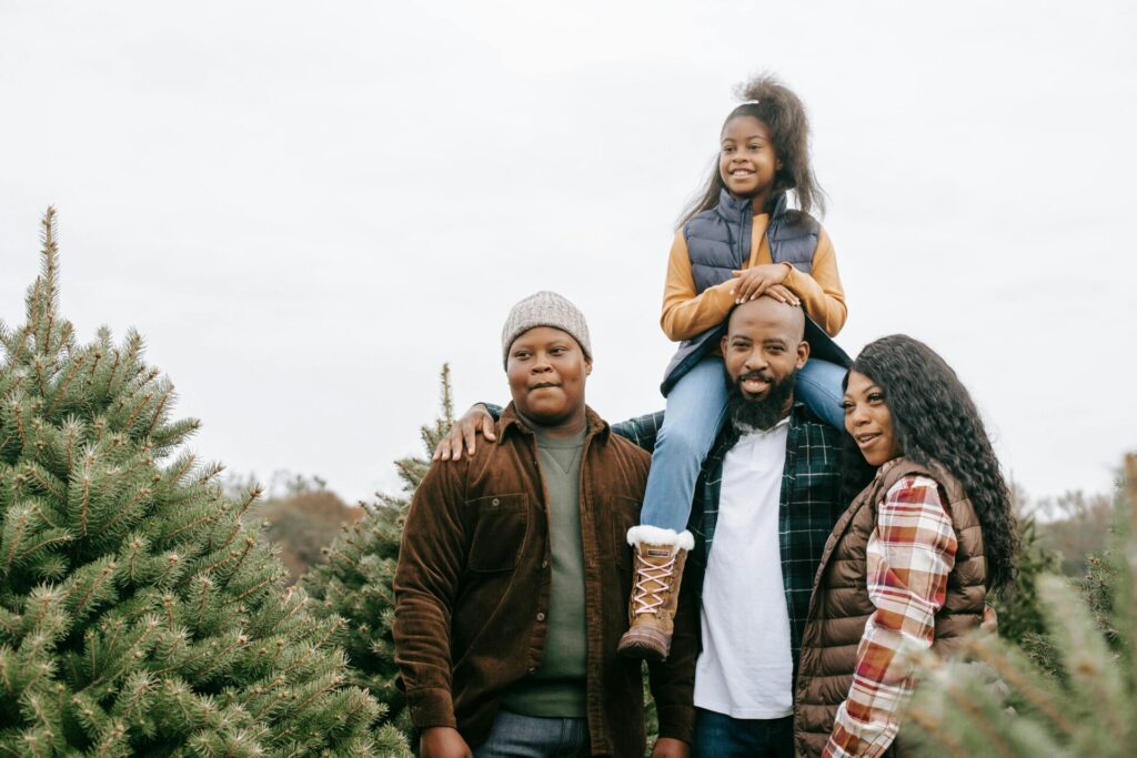 Image of a happy family standing among Christmas trees with child sitting on father's shoulders, showing Is Huntsville Alabama a Good Place to Live for Families.