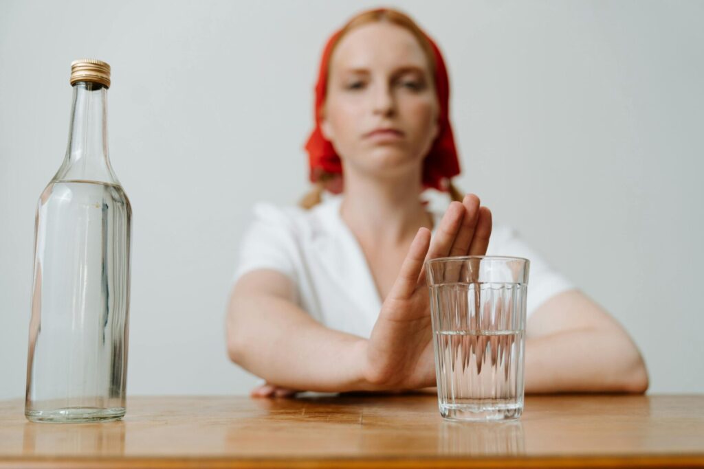 Image of woman in red headscarf refuses a glass of clear liquid on table, pushing it away with her hand, showing women and boundaries.