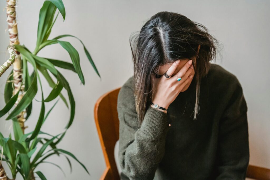Image of women with hand on face, sitting in chair near plant, looking stressed, representing handle seasonal depression in Huntsville winters.