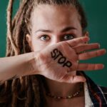 Image of a women with dreadlocks covers mouth with hand showing the word "STOP" written in bold black ink, showing women and boundaries.