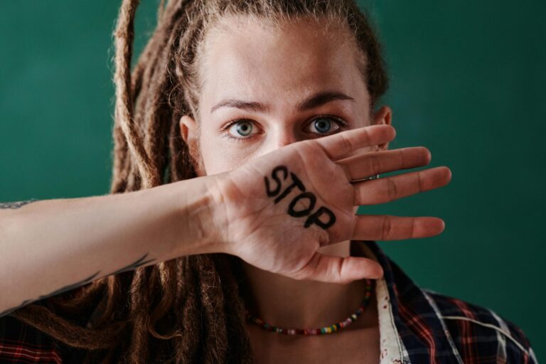 Image of a women with dreadlocks covers mouth with hand showing the word "STOP" written in bold black ink, showing women and boundaries.