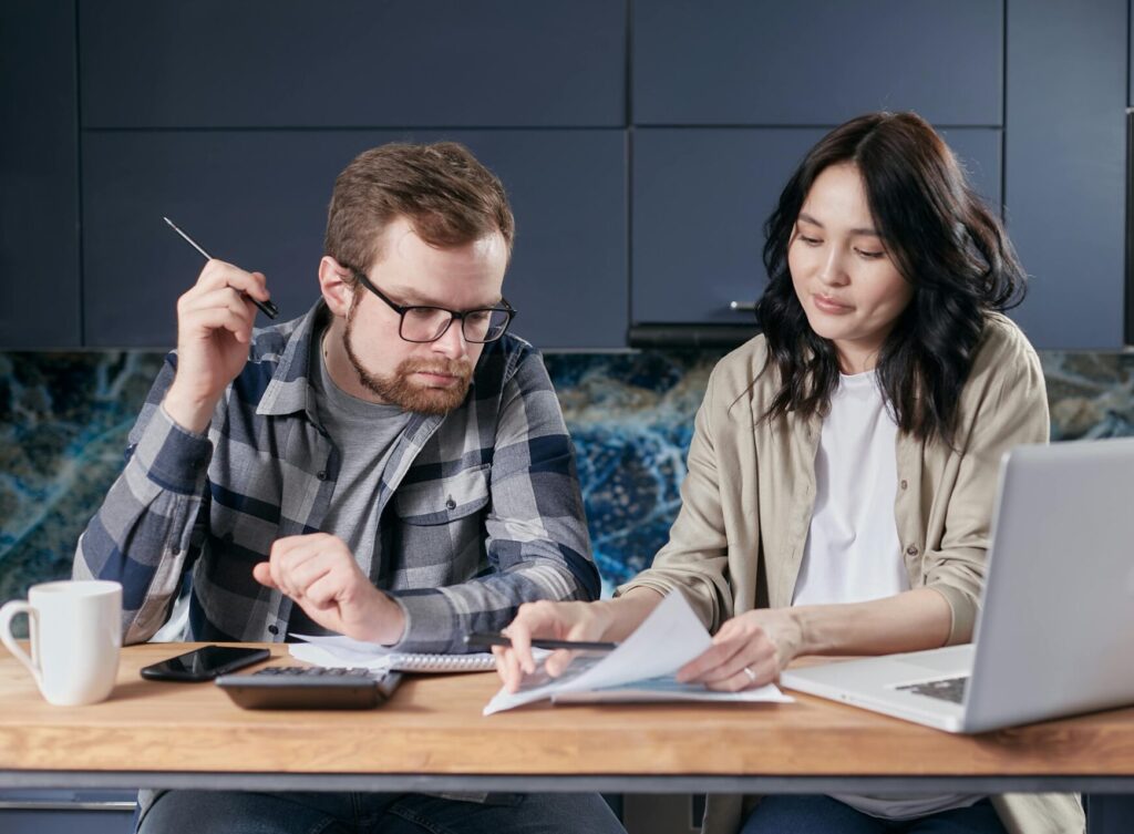 Image of a couple sitting at a table, reviewing documents together with laptop and calculator.