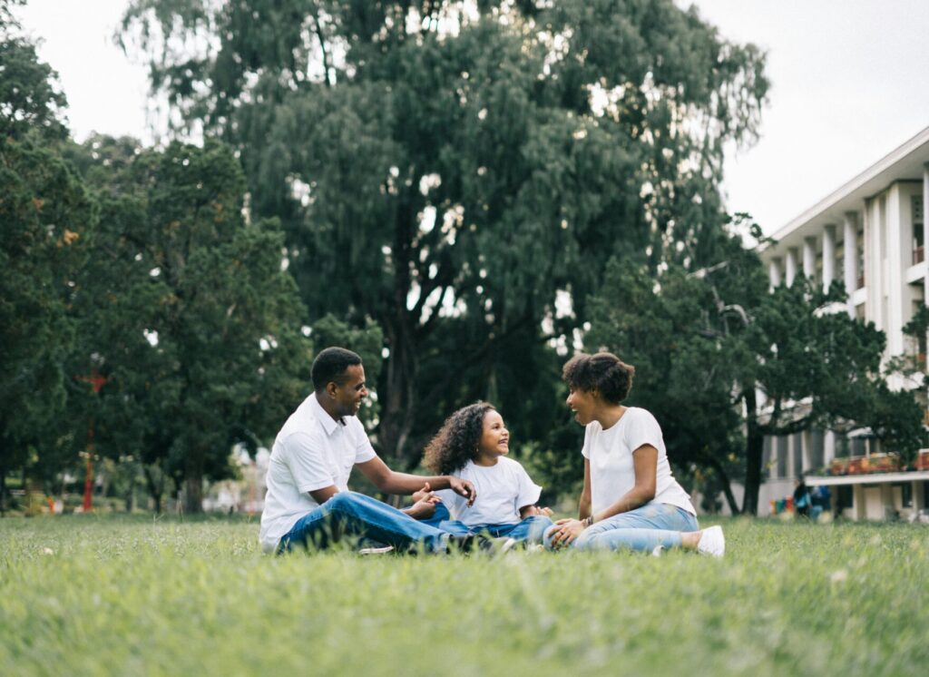 Image of a family sitting on grass in a park, smiling and talking together under large green trees, showing Is Huntsville Alabama safe for black people.